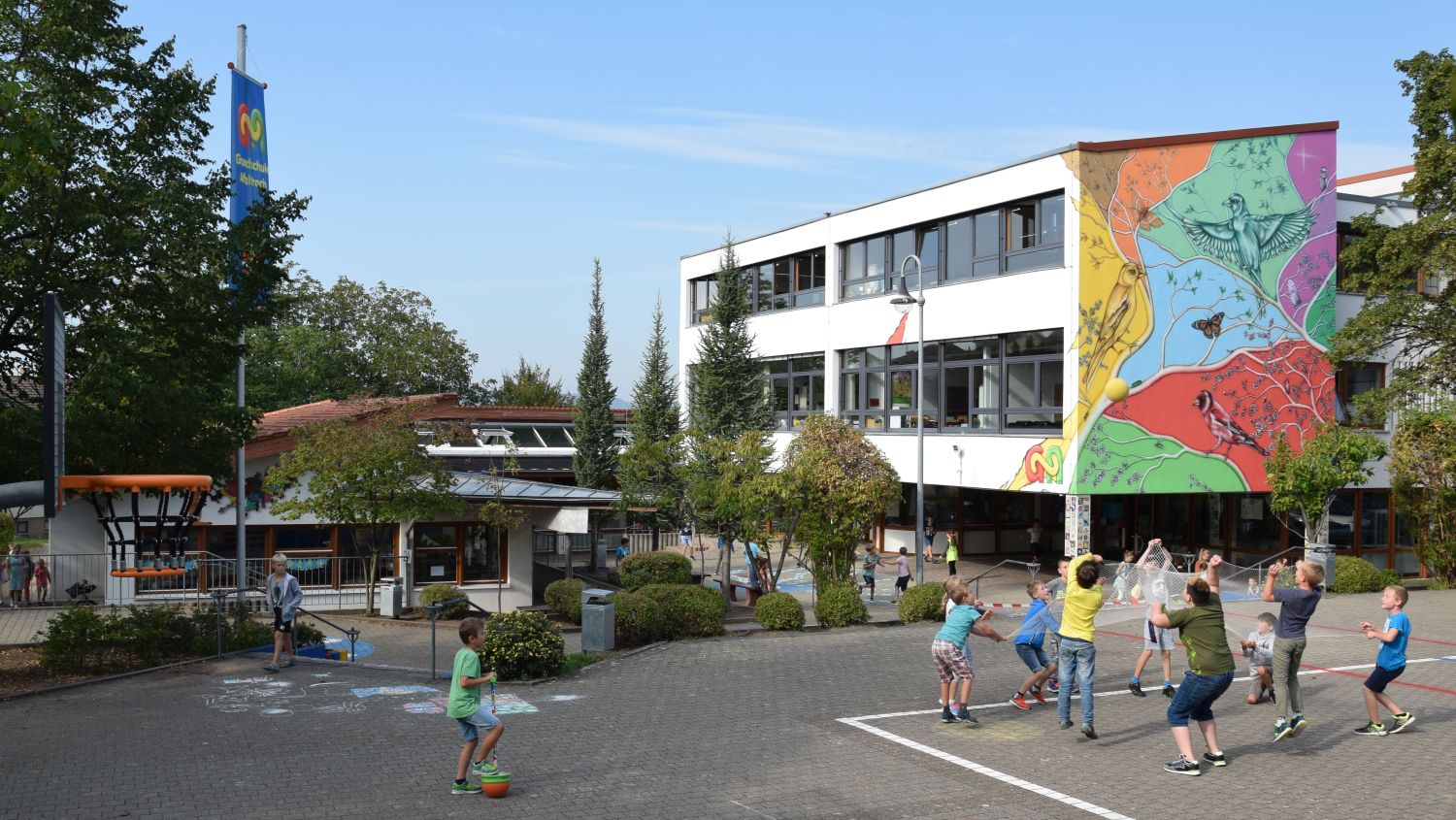 Schulgebäude mit Schulhof und spielenden Kindern